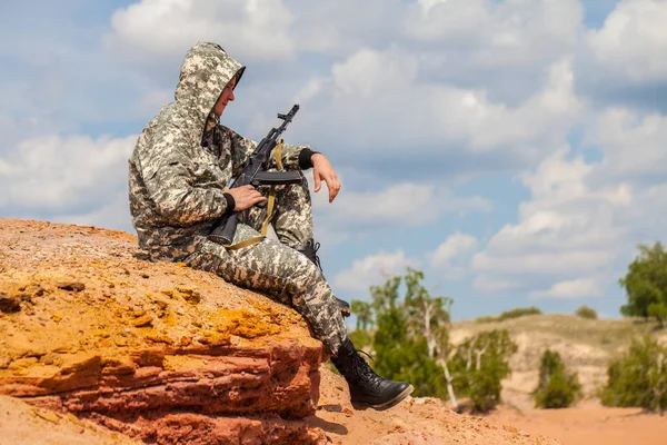 man in camouflage uniform with a weapon in the desert.