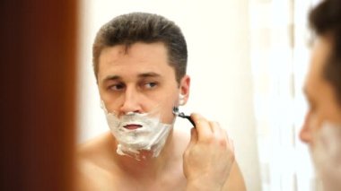 Genç beyaz adam bir güvenlik jilet ile yüzünü tıraş, aynaya yansıma, yan görünüm, yakın çekim