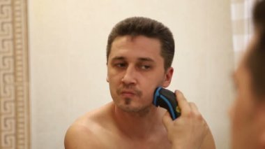 Genç beyaz adam bir elektrikli jilet ile yüzünü tıraş, aynaya yansıma, yakın çekim