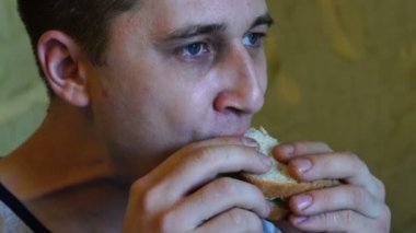 Bir iştah ile sevimli genç aç beyaz adam lezzetli ve sulu sandviç yiyor, dikkatle yakın çekim, yavaş hareket çiğneme