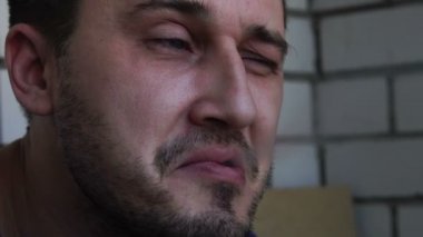 Yüzünde bir inlemek ile genç bir yakışıklı beyaz adam balkonda bir sigara içiyor ve duman, yakın çekim, yavaş hareket havaya uçurmak