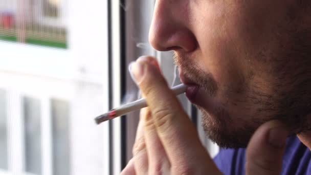 彼の顔に頑固な若いハンサムな白人男性は バルコニーでタバコを吸い クローズアップ スローモーションを爆破 — ストック動画