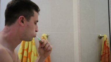 Genç yakışıklı beyaz adam bir diş fırçası ile ayna yansıma içine bakarak dişlerini fırçalama, yakın çekim