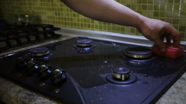 Mutfakta genç bir adamın elleri gazlı sobayı yıkayıp köpük deterjanlı sünger ile yakın çekim