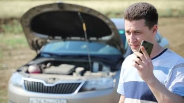 Genç, yakışıklı bir aucasian sürücü kırık bir arabanın yanında duruyor ve servis merkezini çağırır, yakın çekim