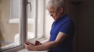 Elderly man using cell phone. Senior man looking and flipping through the photos in her smartphone. He is wearing modern blue polo