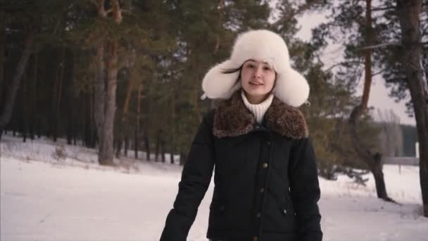Portrait of young beautiful woman in white winter hat walking in winter forest. — Stock video