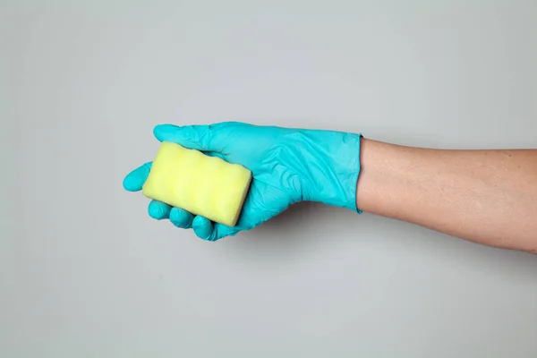 Hand in rubber glove holding cleaning sponge. Hand of chambermaid on gray background. Space for text.