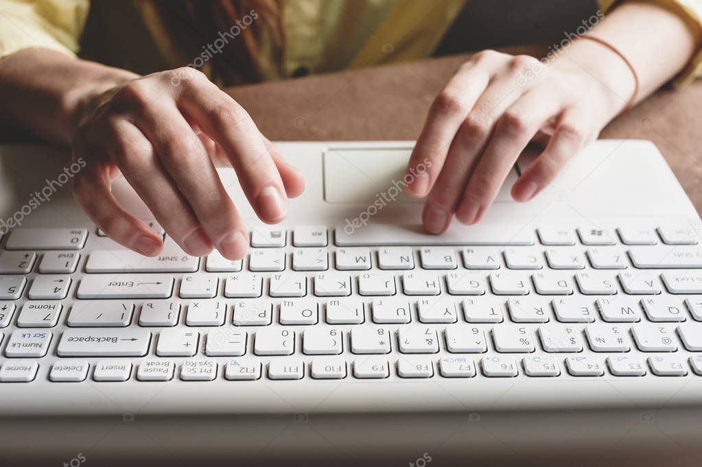 The girl prints on a white computer. Closeup of hands on the keyboard of a computer.