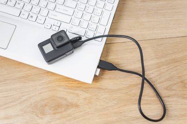Ahşap bir masanın arka planına karşı beyaz bir dizüstü bilgisayara bağlı aksiyon kamerası.