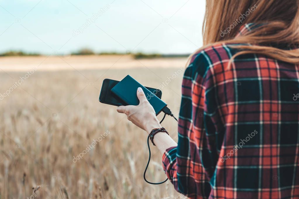 Power Bank in the hand of a girl, against the background of a yellow field.