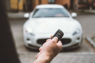 The man opens the car with a keychain, in the background is a white car. clipart