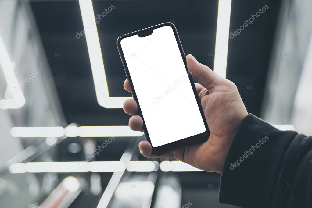 Mock up of a smartphone in hand, on the background of an escalator in a shopping center and luminous lamps.