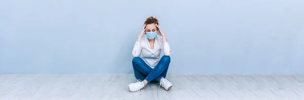 Banner Girl 'ün tıbbi maskesi gri bir duvarın arkasında yerde oturuyor. Coronavirus COVID-19 konsepti