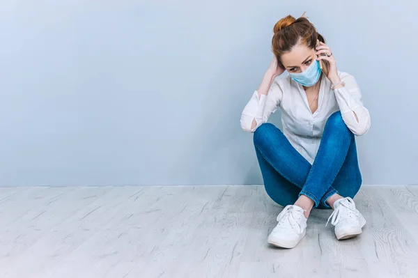 Tıbbi maskeli bir kız yerde oturmuş telefonda konuşuyor. Coronavirus COVID-19 teması