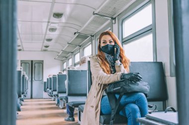 Kızıl saçlı bir kız telefonda konuşuyor, bir tren vagonunda, siyah bir tıbbi maskeyle.