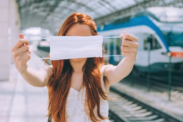 駅で医療マスクを手にした少女 現代の列車を背景に — ストック写真