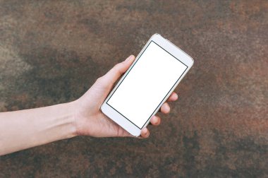 Beyaz bir akıllı telefonun kopyası, bir kızın elinde, eski paslı bir metal masanın arka planında..