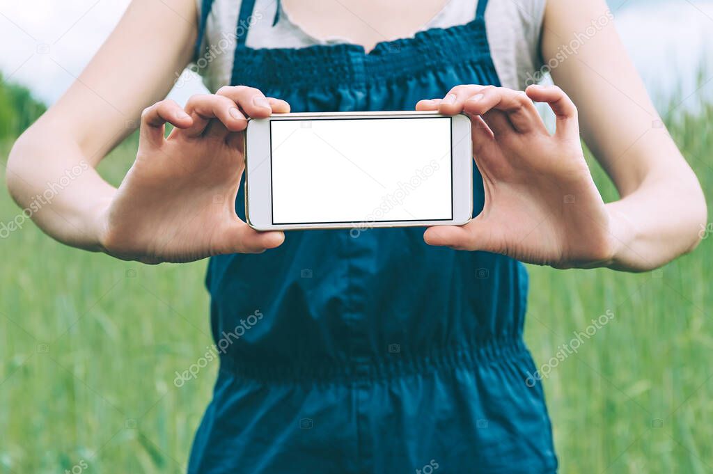 Mock up of a smartphone in the hands of a girl farmer, against the background of a green field.