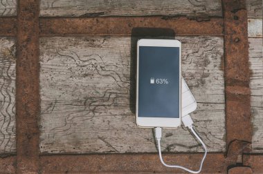 Telefonu elektrik bankasından şarj etmeye yakın çekim. Eski tahta bir sandığın üzerinde.