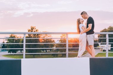 Adam ve kız gün batımında öpüşüyorlar.