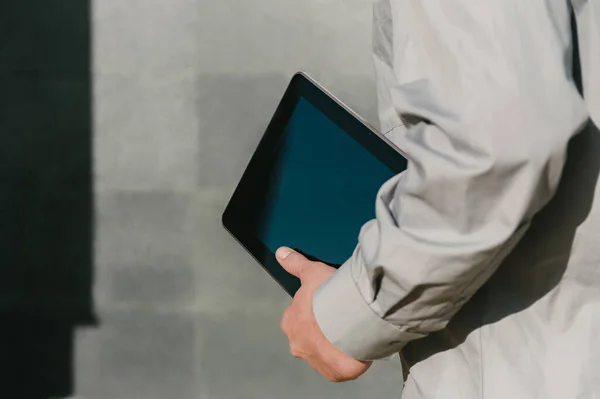 Tablet yürüyen bir adamın elinde, yakın plan. Beton bir duvarın arka planına karşı gölgesi olan