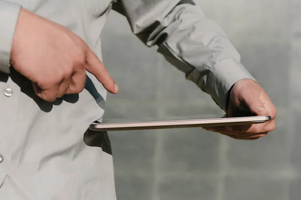 Finger in front of tablet screen, in hand, Business man. against the background of a concrete wall