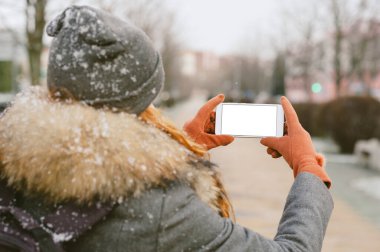 Bir kızın elindeki akıllı telefonun maketi gibi. Kar yağan bir şehrin arka planına karşı