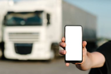 Bir adamın elinde akıllı telefon taklidi yapmak gibi. Kamyonların arka planına karşı. Lojistik kavramı