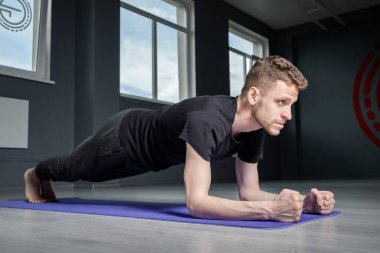 Genç bir adam spor salonunda dirseklerin üzerinde bir kalasın üzerinde duruyor. Erkek egzersizi..