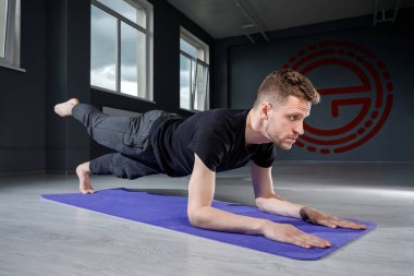 Genç bir adam, bir ayağı spor salonunda kaldırılmış dirseklerin üzerinde bir tahta üzerinde duruyor. Erkek egzersizi..