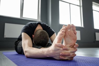 Spor salonundaki yoga minderinde bacak esnetme egzersizi yapan genç bir adam. Seçici odak.