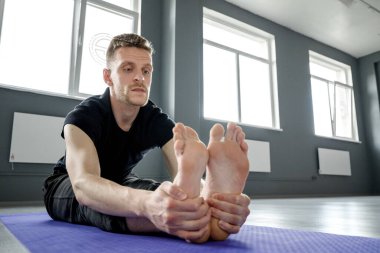 Spor salonundaki yoga minderinde bacak esnetme egzersizi yapan genç bir adam. Seçici odak.