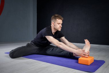 Genç adam yoga minderiyle bacağını esnetiyor..