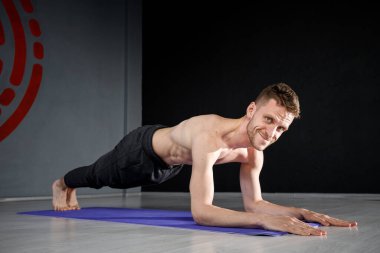 Genç atletik adam yoga minderinin ön kolunda duruyor..