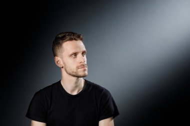 Genç adam, siyah arka planda düşünceli bir şekilde yana bakıyor..