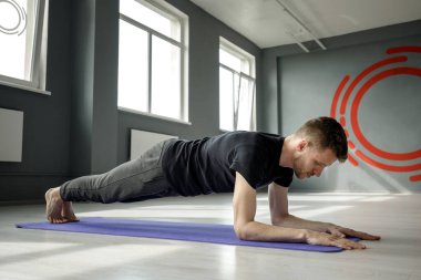 Genç bir adam spor salonunda dirseklerin üzerinde bir kalasın üzerinde duruyor. Erkek egzersizi..