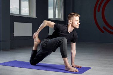 Spor salonundaki yoga minderinde bacak esnetme egzersizi yapan genç adam..