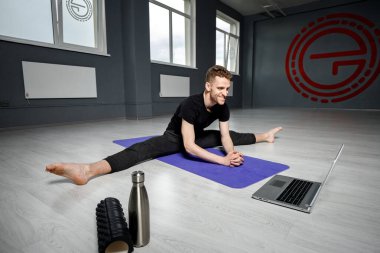 Genç, atletik adam dizüstü bilgisayarın önünde geriniyor. Online yoga dersi.