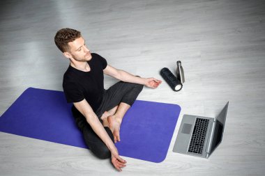Genç, atletik adam dizüstü bilgisayarın önünde meditasyon yapıyor. Online yoga dersi.