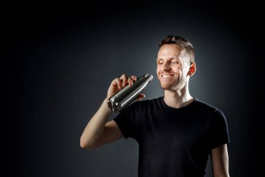 Siyah arka plandaki genç gülen adam fitness şişesinden su içiyor..