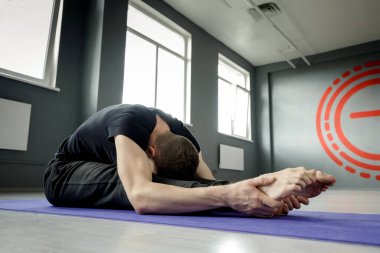 Spor salonundaki yoga minderinde bacak esnetme egzersizi yapan genç bir adam. Seçici odak.
