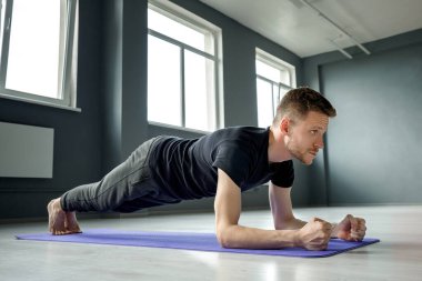 Genç bir adam spor salonunda dirseklerin üzerinde bir kalasın üzerinde duruyor. Erkek egzersizi..