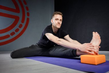 Genç adam yoga minderiyle bacağını esnetiyor. Seçici odak.