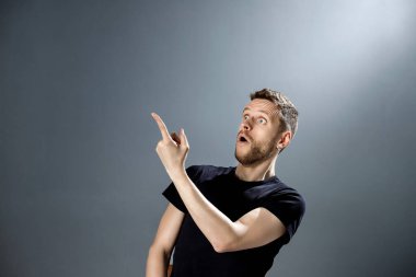 Şaşırmış yüzlü genç adam gri arka planda ilginç bir şey gösteriyor..