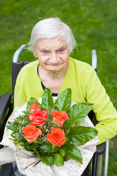 残疾老年妇女坐在轮椅上 收到鲜花花束为她的生日 — 图库照片