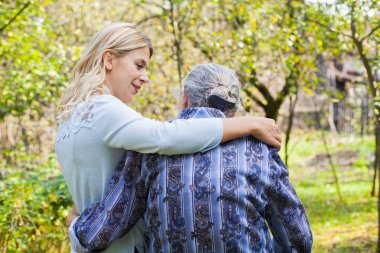 Genç kadın kucaklayan yaşlı kadın bahçede yürürken