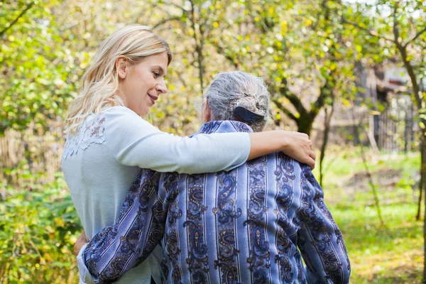 Genç kadın kucaklayan yaşlı kadın bahçede yürürken