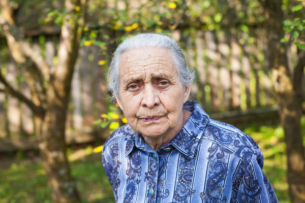 Portrait of old wrinkled lady wearing blue dress, walking in the garden on summertime