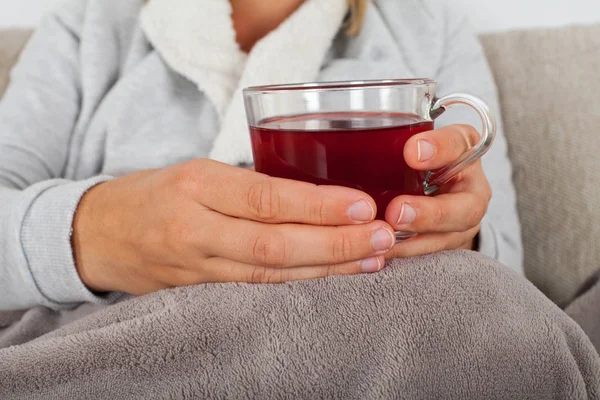 关闭的图片的生病的妇女拿着一杯热茶 而坐在沙发上裹着温暖的毯子 — 图库照片